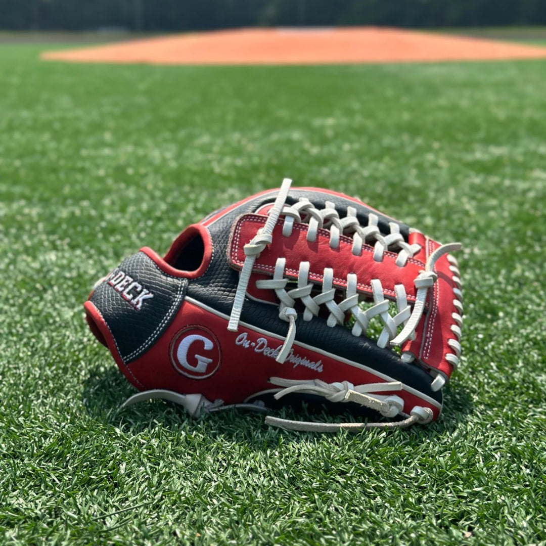 An On-Deck Originals branded black, white and red Grace Glove Co. baseball glove, laying palm down. on a turf field. In the background is a pitcher's mound and a turf infield