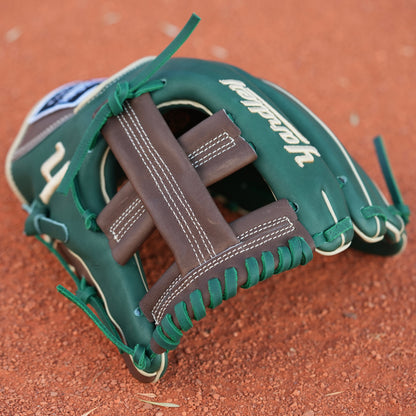 A baseball glove on a dirt field. The glove is primarily green with brown and beige accents, featuring intricate stitching and a patch with text on the wrist area. The letter Y is stitched on the side, indicating Yardley Sports.