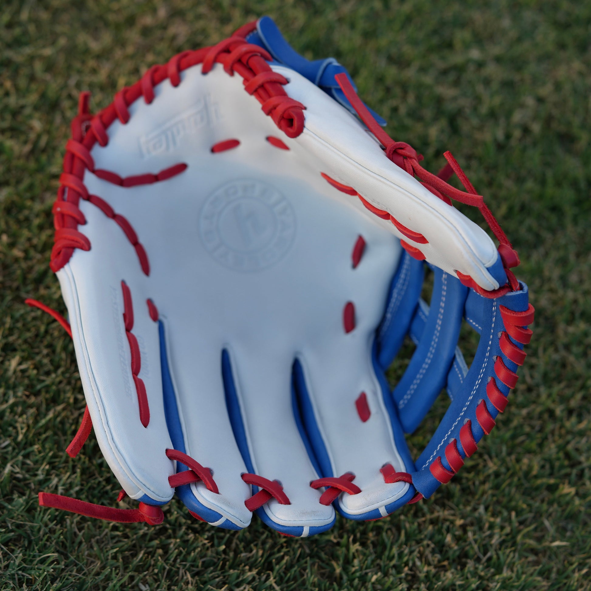  A red Yardley baseball glove with black and white stitching and black laces on a grass field. The glove has a "Y" logo on the thumb area, showcasing its unique design. The webbing is an H-web style