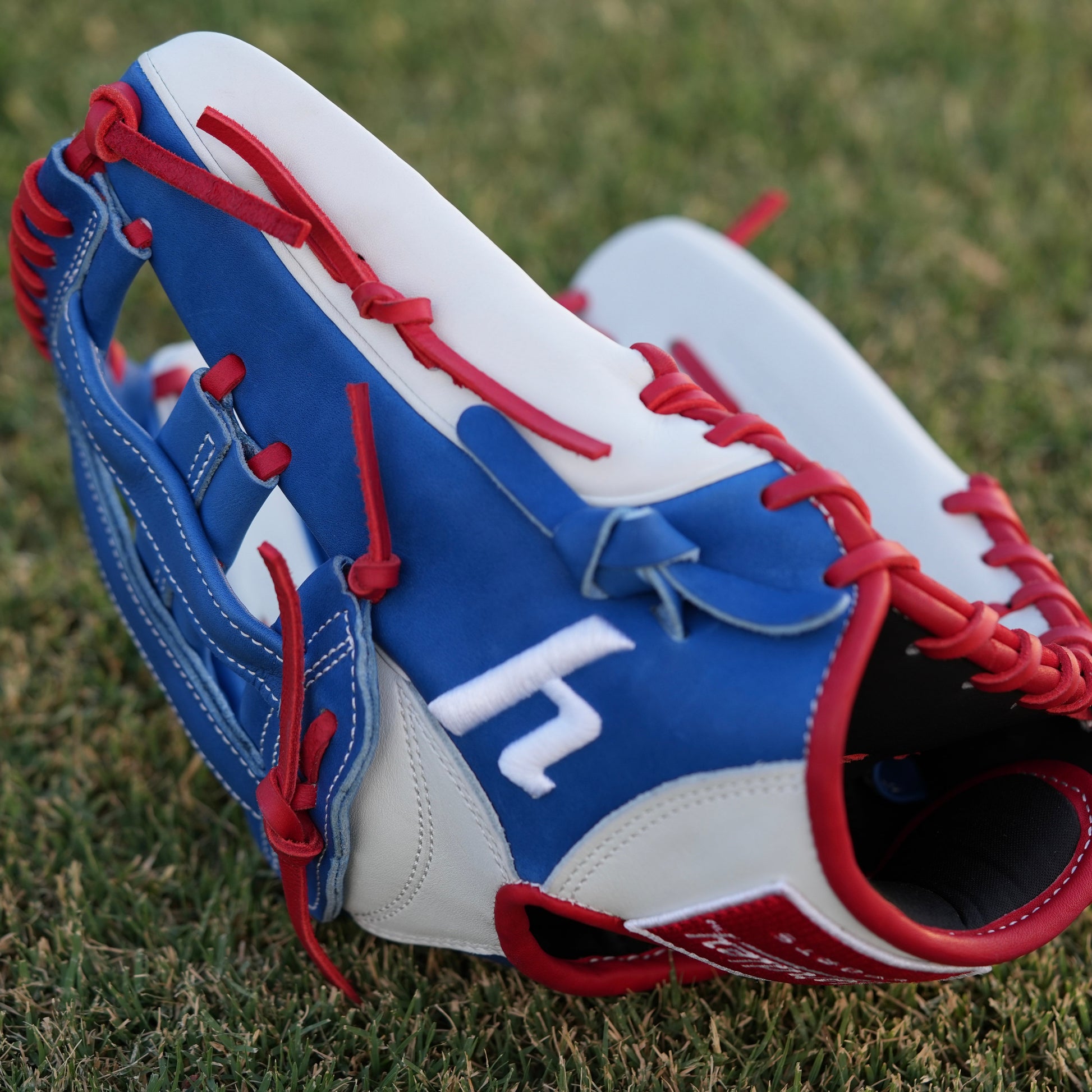  A red Yardley baseball glove with black and white stitching and black laces on a grass field. The glove has a "Y" logo on the thumb area, showcasing its unique design. The webbing is an H-web style