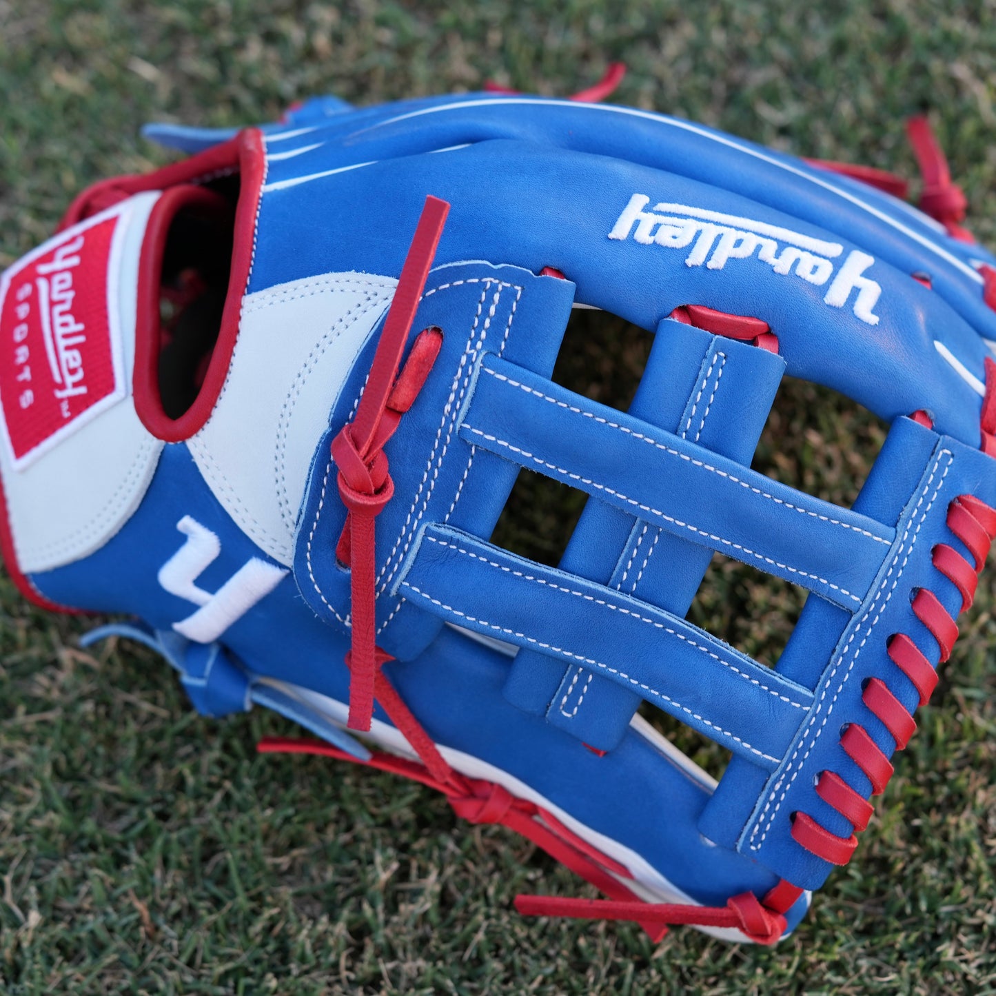  A red Yardley baseball glove with black and white stitching and black laces on a grass field. The glove has a "Y" logo on the thumb area, showcasing its unique design. The webbing is an H-web style