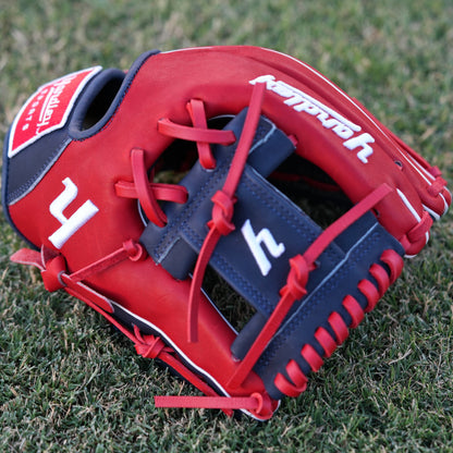 A red and navy blue baseball glove lying on grass, featuring the Yardley Sports logo and branding. The glove has red laces, white embroidered text, including the letter "Y." The design and color scheme highlight the premium quality and craftsmanship associated with Yardley Sports.