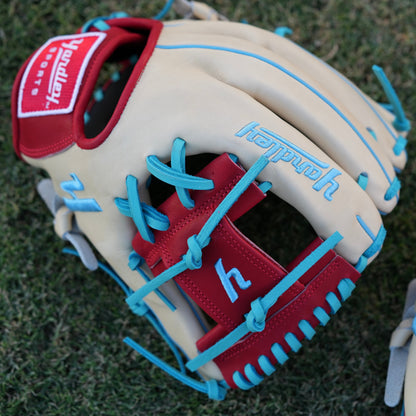 A stylish beige baseball glove with blue laces and accents, red trim around the wrist, and "Yardley" embroidered in blue on the back of the fingers. The glove rests on a grassy field, showcasing its vibrant design and quality craftsmanship.