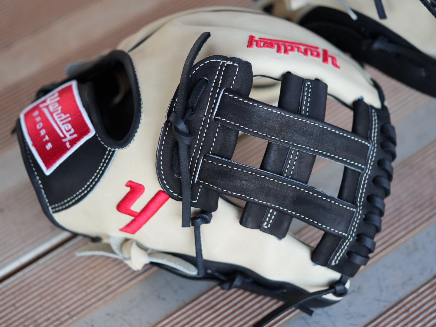 Beige baseball glove with black stitching and red "Yardley" branding, placed on a metal surface. The glove showcases a sleek design with fine craftsmanship.