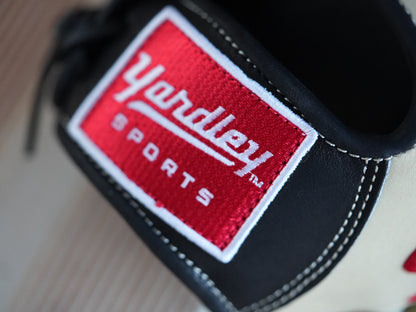 Beige baseball glove with black stitching and red "Yardley" branding, placed on a metal surface. The glove showcases a sleek design with fine craftsmanship.