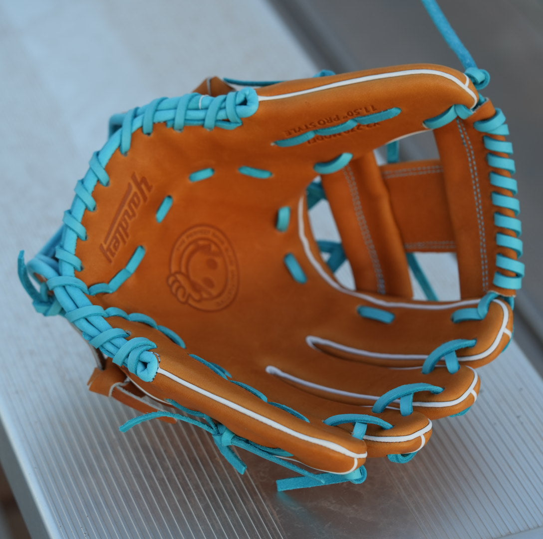 A brown and blue Yardley baseball glove with blue laces and stitching sits on a metallic surface. The glove features the letter Y stitched in blue on the thumb area and another letter Y on the webbing. The modern, stylish design showcases a unique color combination and intricate craftsmanship.