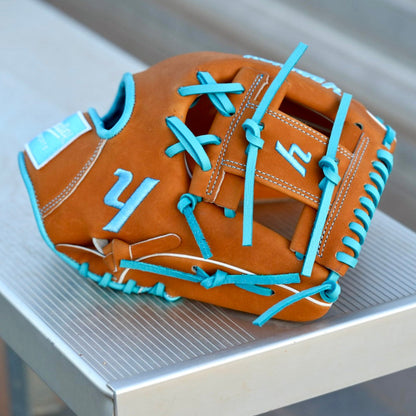 A brown and blue Yardley baseball glove with blue laces and stitching sits on a metallic surface. The glove features the letter Y stitched in blue on the thumb area and another letter Y on the webbing. The modern, stylish design showcases a unique color combination and intricate craftsmanship.