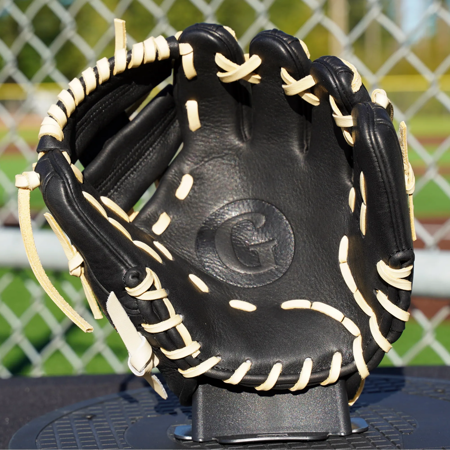 A 9.5" Grace training glove, the palm of the glove against a turf baseball field, prominently featuring black leather and blonde lacing