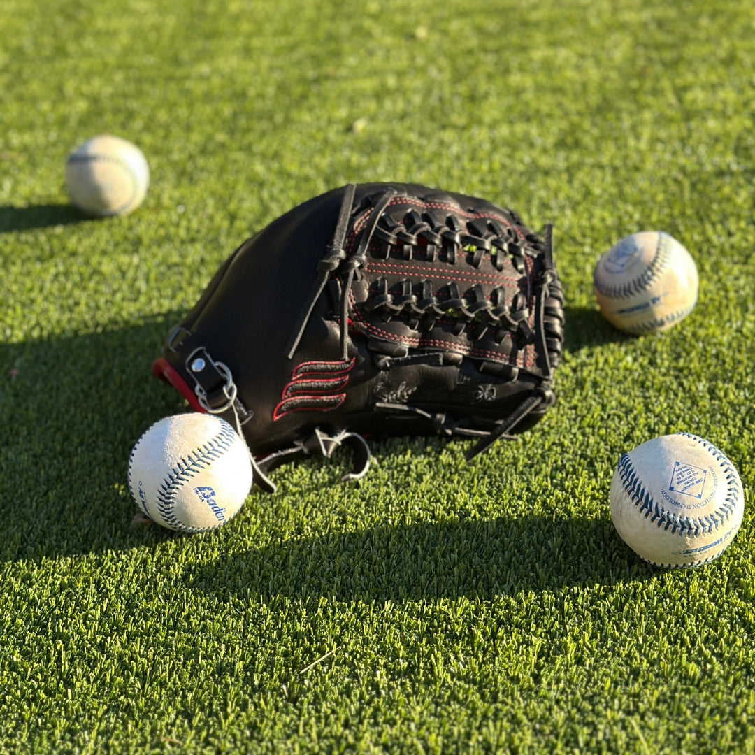 All black with red accent closed back semi-custom baseball glove. The Phantom, set on a turf baseball field