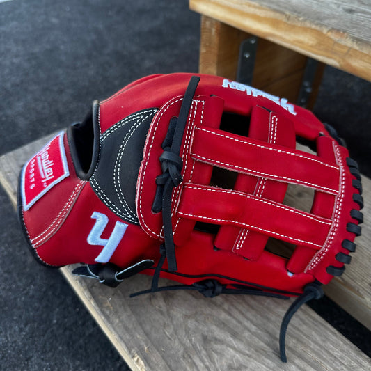  A red Yardley baseball glove with black and white stitching and black laces on a wooden bench. The glove has a "Y" logo on the thumb area, showcasing its unique design. The webbing is an H-web style