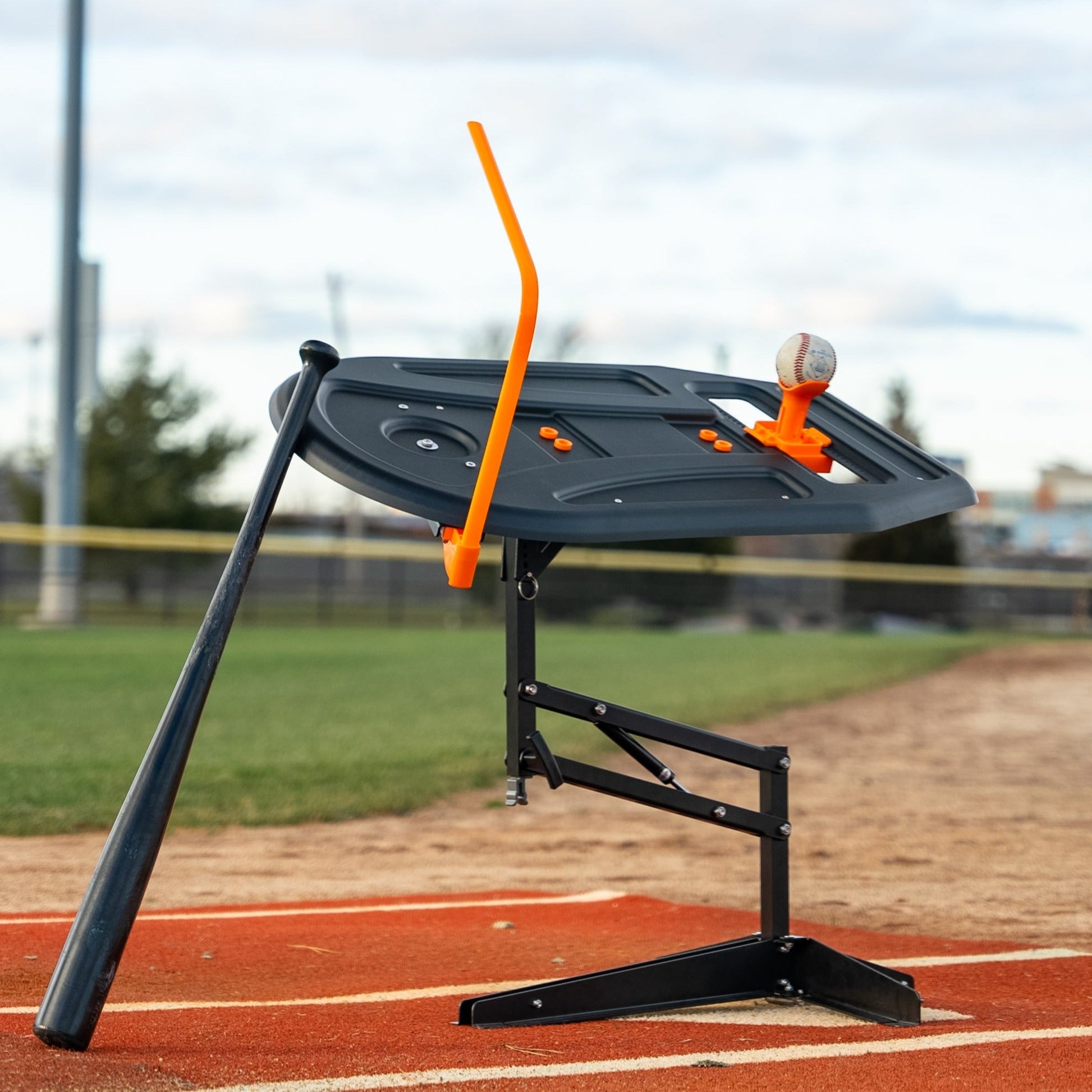 A black wooden baseball bat leaning against the Perfect Swings USA swing path trainer on a baseball field