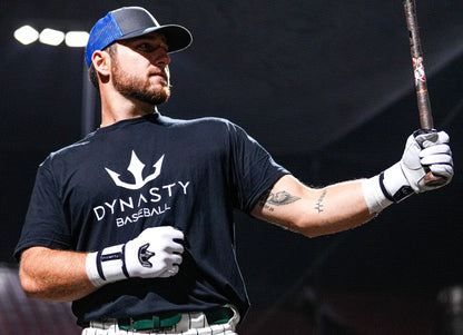 A baseball player holding a baseball bat, wearing dynasty baseball batting gloves in white, along with the dynasty baseball t-shirt