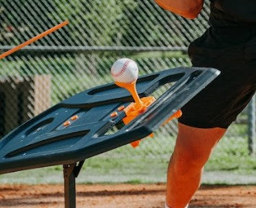 The tee topper attached to the Perfect Swings USA swing-path trainer. A batter is taking a swing in the background on a baseball field