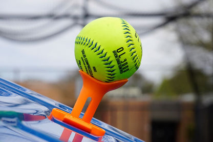 A yellow softball placed on top of the tee topper in an outdoor setting