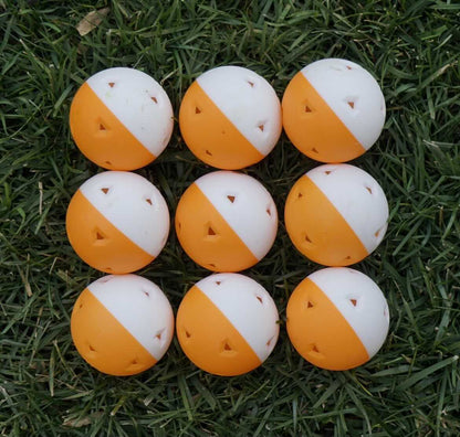 9 training wiffle balls, colored orange and white, against a natural grass background